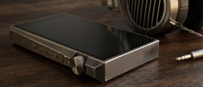 Hi-Fi плеер с металлическим корпусом рядом с полноразмерными наушниками на столе