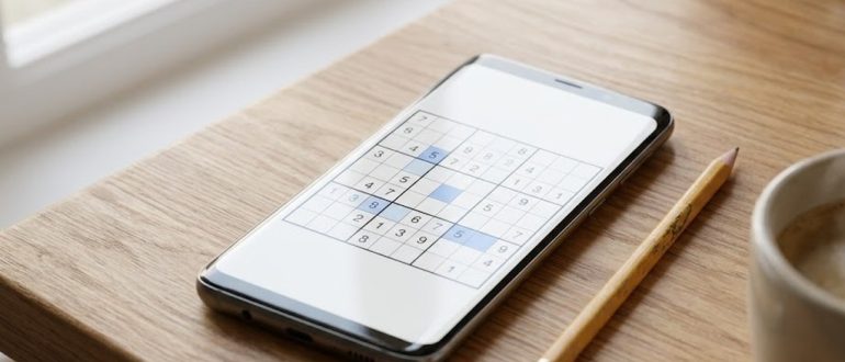 Смартфон на Android с наполовину решённой сеткой судоку на деревянном столе